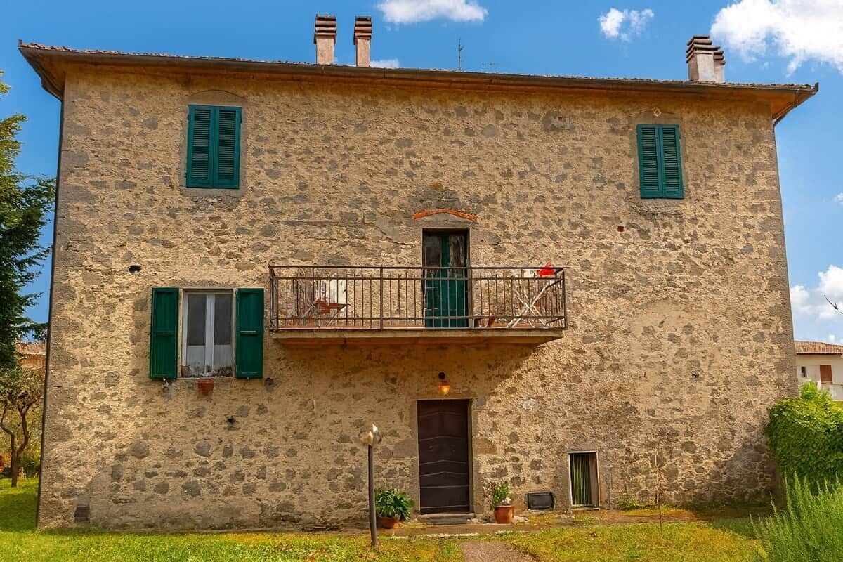 Un bâtiment en pierre doté d’un balcon, d’une porte et d’un petit jardin.
