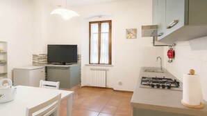 A compact kitchen with a TV, a window, a stove, and a dining area. - Casa Maria Amiata: A Cozy House Amid Nature and Comfort (San Lorenzo)