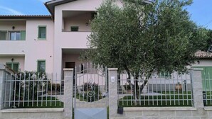A multi-story building with a gated entrance, a tree in front, and a stone wall. - Everything is just a bike ride away! 10 minutes to the beach with free (Grosseto)