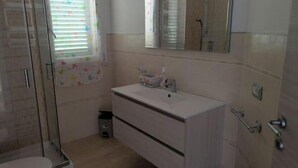 A bathroom with a glass shower enclosure, a sink with a mirror, and a small trash bin. - Everything is just a bike ride away! 10 minutes to the beach with free (Grosseto)