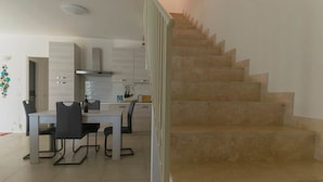 A modern kitchen with a dining table and chairs, a staircase, and a white interior. - To complete (Grosseto)