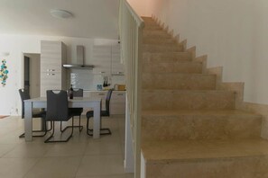A modern kitchen with a dining table and chairs, a staircase, and a white interior. - To complete (Grosseto)