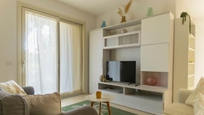 A living room with a sofa, a coffee table, a TV, and a sliding glass door. - To complete (Grosseto)
