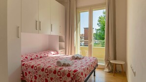 A bedroom with a bed, a small table, and a balcony with curtains. - To complete (Grosseto)