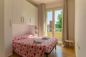 A bedroom with a bed, a small table, and a balcony with curtains. - To complete (Grosseto)