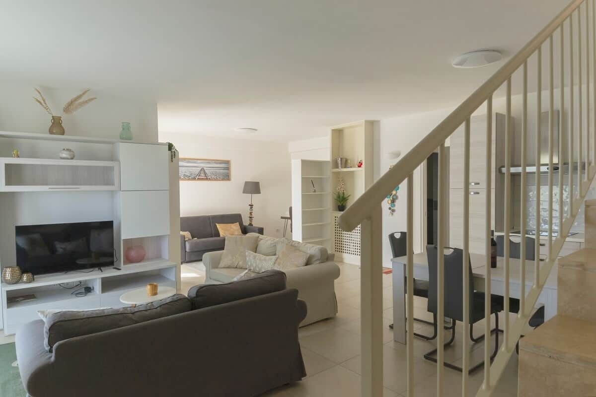Un salon moderne doté d’un téléviseur à écran plat, de canapés, d’une table basse et d’un escalier menant à un espace repas.