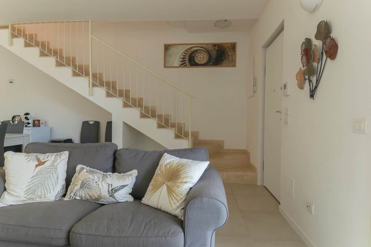 Un salon avec un canapé gris, un escalier et un mur décoré de différents objets.