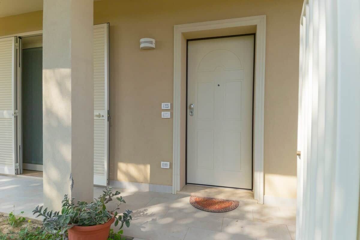 A beige exterior with a white door, a potted plant, and a doormat.