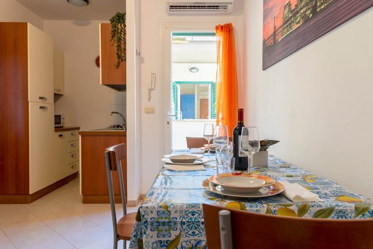 A dining area with a table set for two, a kitchen in the background, and a view through a door.