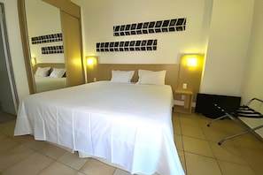 Ein Hotelzimmer mit einem großen Bett, zwei Nachttischen, einem Spiegel und Wandleuchten.