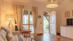 Ein gemütliches Wohnzimmer mit einer Couch, einem Tisch, einer Lampe und Blick ins Freie durch eine Tür.