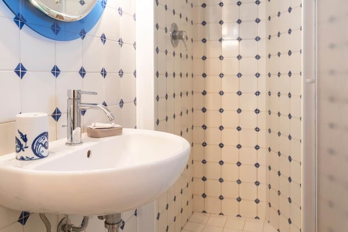 A bathroom with a white sink, a mirror, and a shower with patterned tiles.