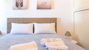 Ein ordentlich bezogenes Bett mit weißen Kissen und Handtüchern, ein Korbhaupt und zwei an der Wand hängende Bilder.