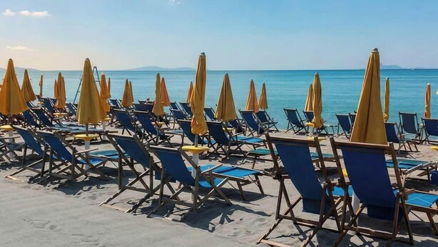 Ein Strand mit blauen Liegestühlen und gelben Sonnenschirmen.