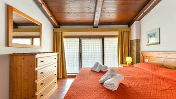 Una camera da letto con una cassettiera in legno, un letto con copripiumino arancione, uno specchio, una lampada e una finestra con tende.