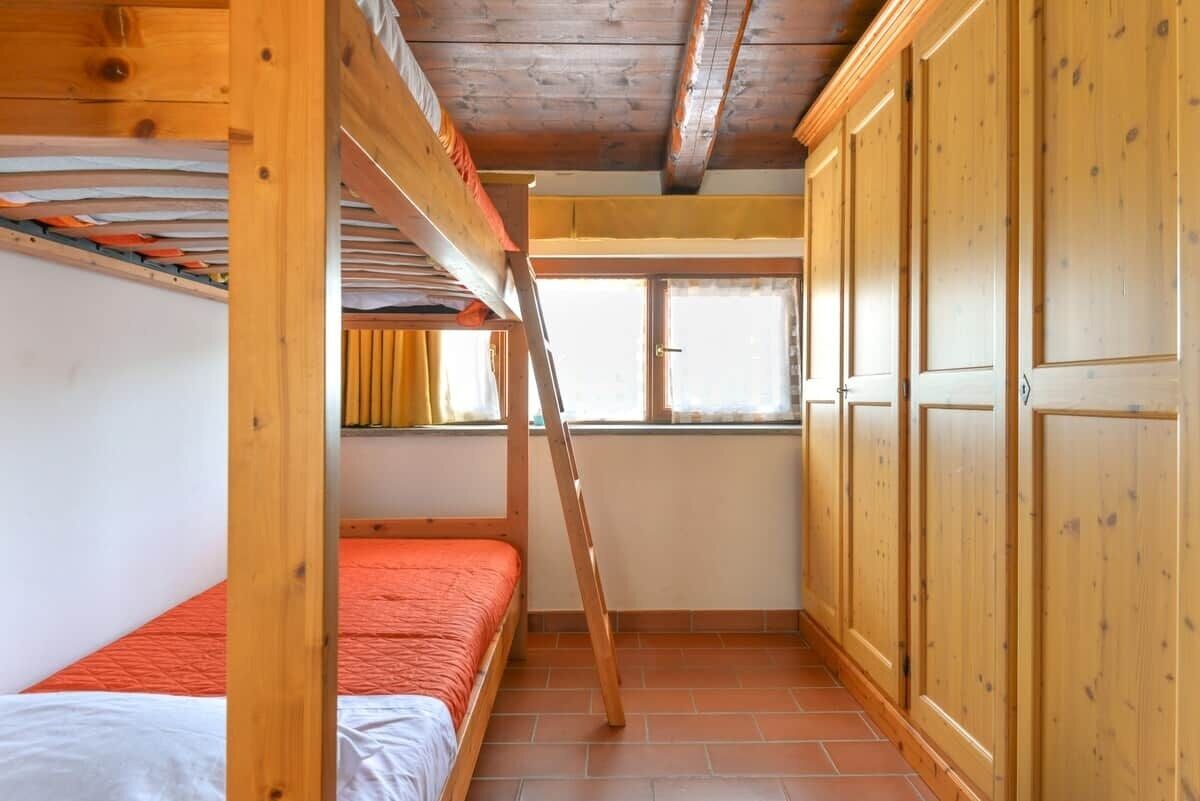 A room with bunk beds, wooden wardrobe, and a window with curtains.