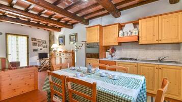 Una cucina rustica con mobili in legno, un tavolo da pranzo apparecchiato con sedie e un televisore nell'angolo.