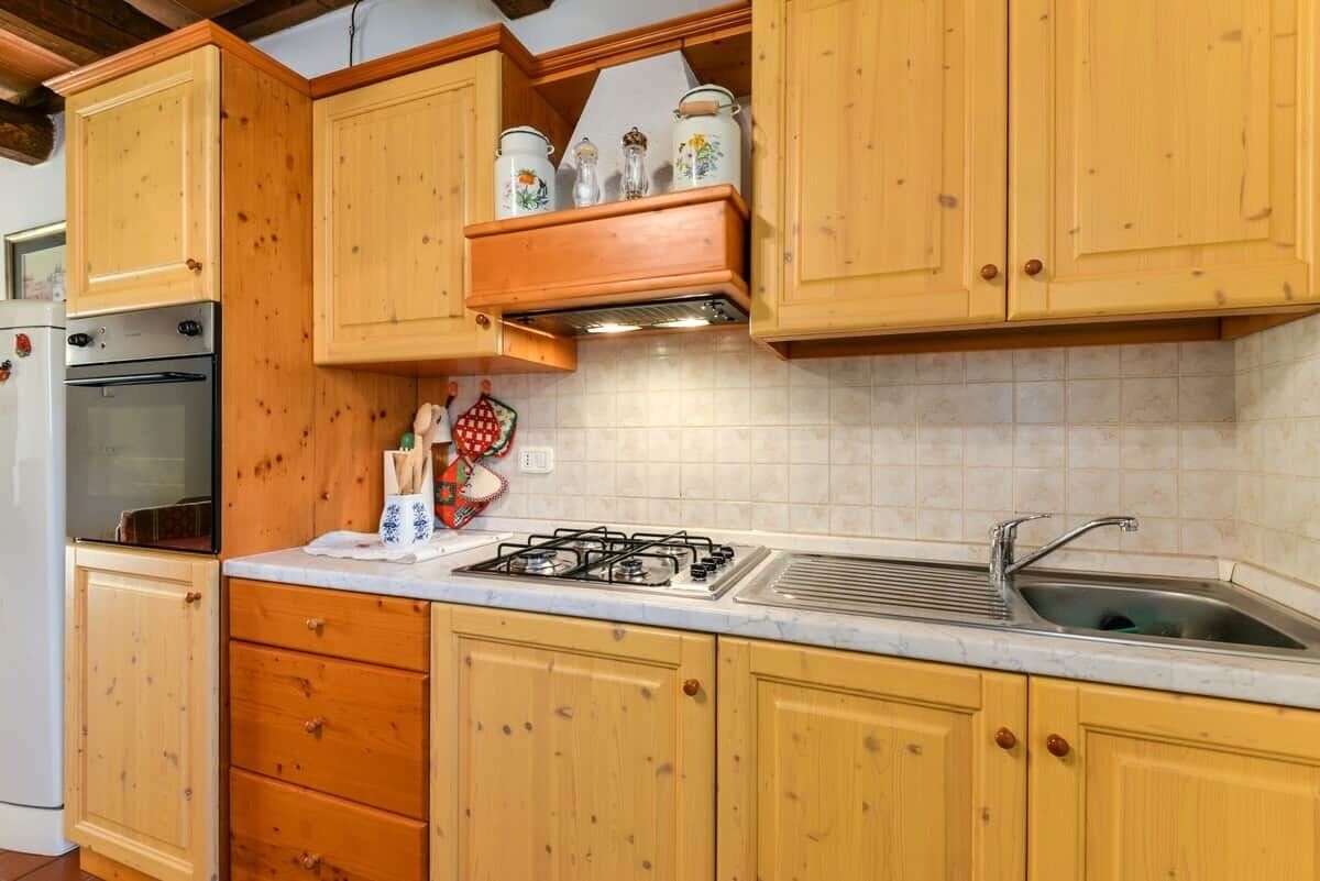 Een keuken met houten kastjes, een gasfornuis, een spoelbak en een koelkast.