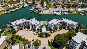 A marina with boats docked, a central swimming pool, and a building with a symmetrical design. - South End Waterfront Condo | Walk to Beach (Marco Island)