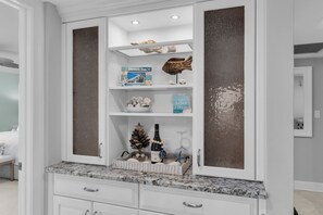 A white cabinet with shelves containing decorative items, a small Christmas tree, and a bottle of wine. - South End Waterfront Condo | Walk to Beach (Marco Island)