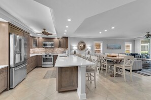 A modern kitchen with built-in appliances, a dining area with a large island, and a living room with a sofa and a painting. - South End Waterfront Condo | Walk to Beach (Marco Island)