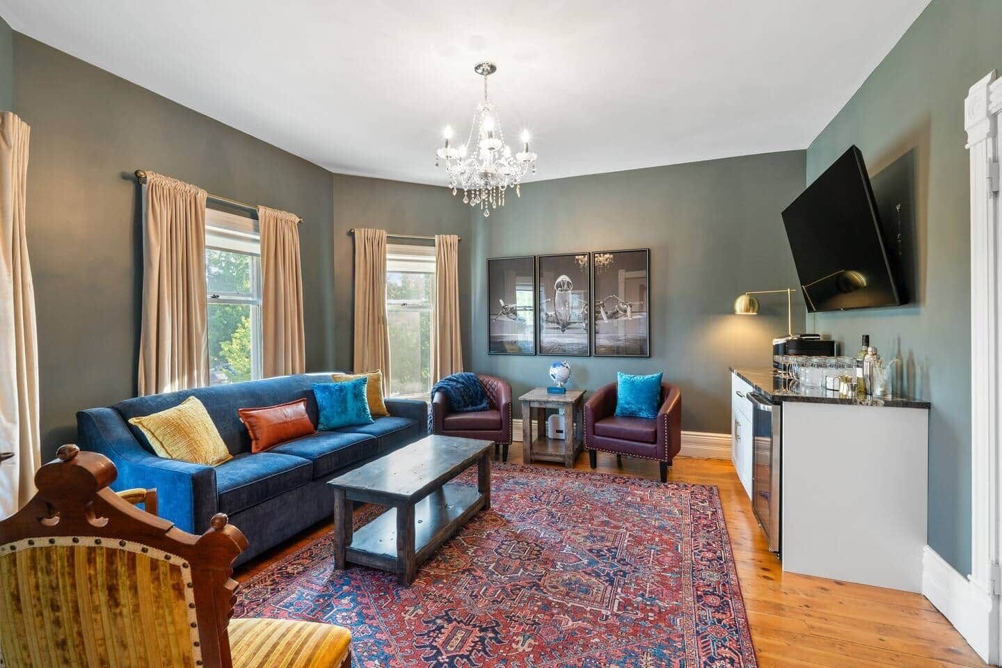 A living room with a sofa, armchairs, a coffee table, a chandelier, a TV, and a bar area.