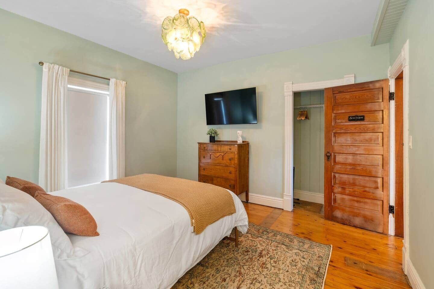 A bedroom with a bed, a dresser, a television, and a door leading to a closet.