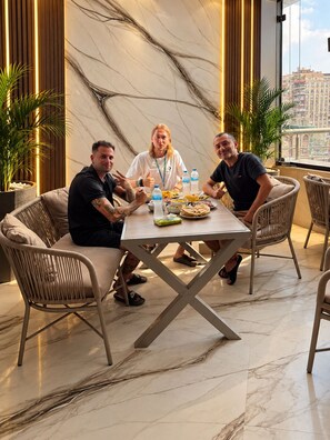 A group of people seated at a table with a city view, in a room with a marble floor and modern furnishings. - Grand Pyramids Hotel (Giza)