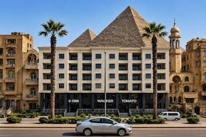 A hotel with a pyramid-shaped roof, palm trees, and a minaret. - Grand Pyramids Hotel (Giza)