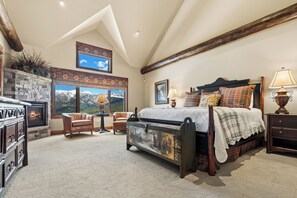 A bedroom with a fireplace, a bed, a chair, and a view of mountains.