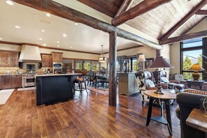 A spacious kitchen with wooden beams, a dining area with a large island, and a living room with a fireplace.