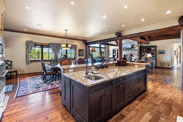 A spacious kitchen with a large island, wooden flooring, and a view of mountains through the windows.