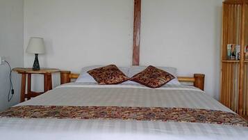 A bed with a patterned bedspread, two decorative pillows, a wooden headboard, a nightstand with a lamp, and a wooden wardrobe.