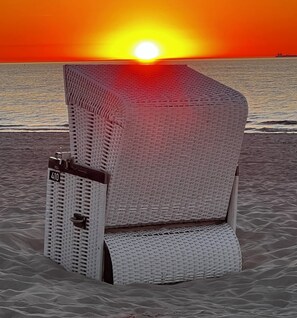Ein Liegestuhl mit einer Nummer am Strand, im Hintergrund ein Sonnenuntergang.