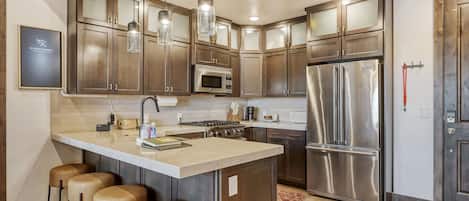 Una cocina moderna con electrodomésticos de acero inoxidable, armarios de madera y una isla central con taburetes.