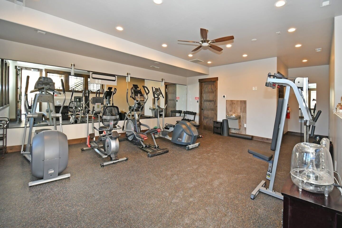A gym with various exercise equipment, a ceiling fan, and a large mirror.