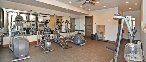 Un gimnasio con diferentes equipos de ejercicio, un ventilador de techo y un espejo grande.