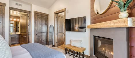 A bedroom with a bed, a bench, a fireplace, and a mirror.
