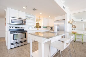 A modern kitchen with a central island, stainless steel appliances, and white cabinetry. - Phoenix X 1506 3 Bedroom Condo (Orange Beach)