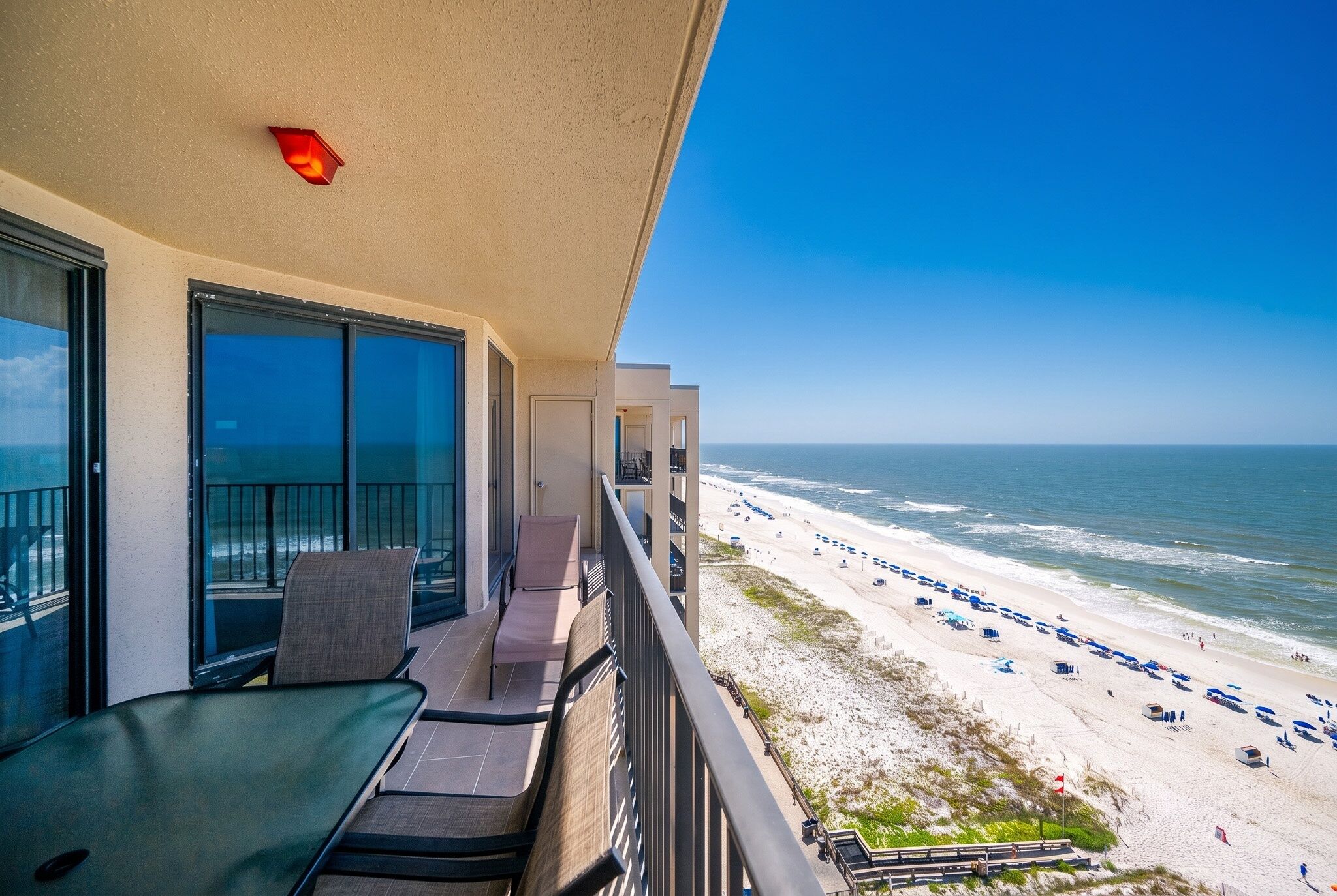 A balcony with a view of the beach, outdoor seating, and a clear sky.