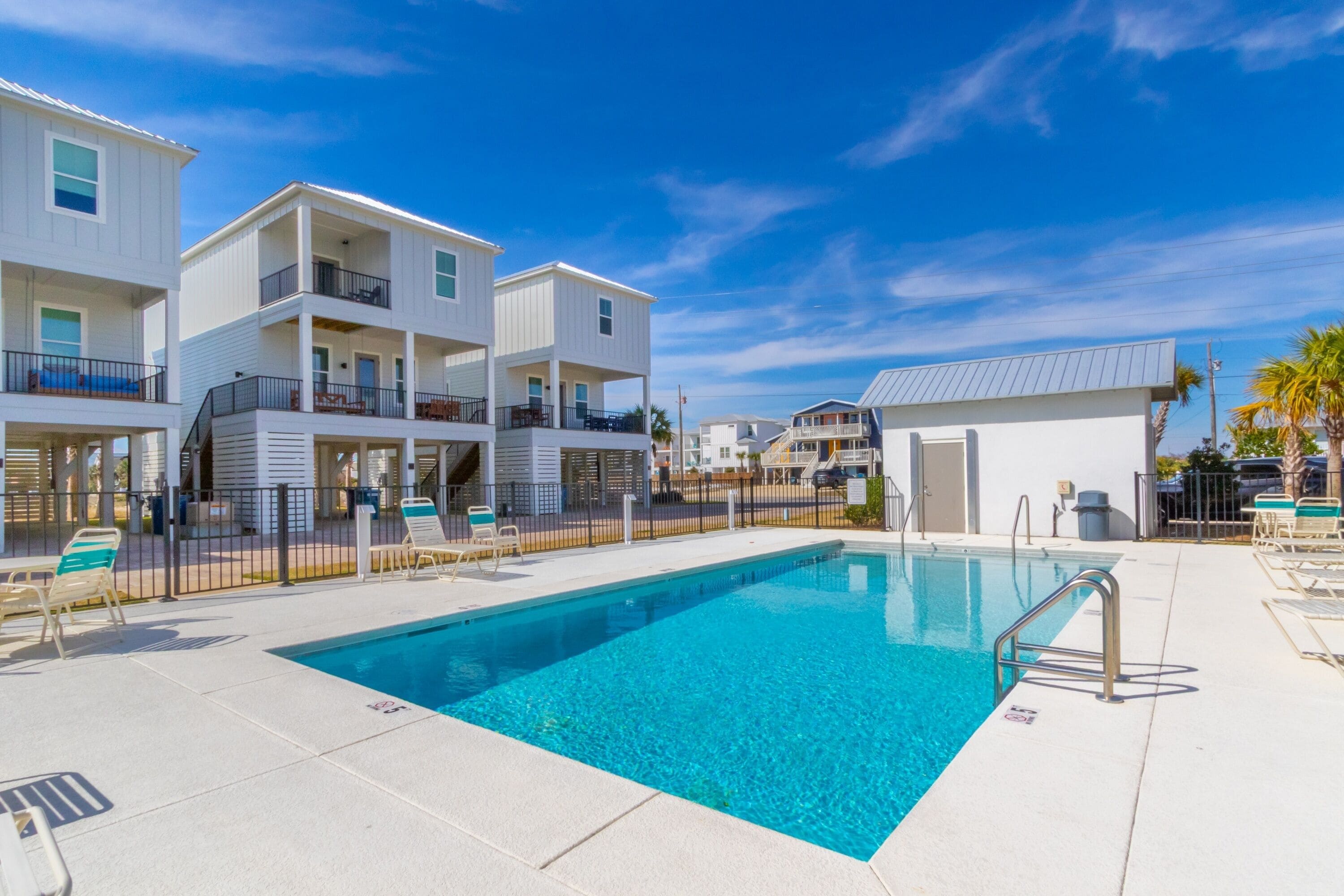 A swimming pool with a metal ladder, lounge chairs, and a building with balconies.