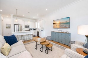 A modern living room with a sofa, a coffee table, and a dining area with stools. - Endless Summer 161 4 Bedroom Home (Gulf Shores)