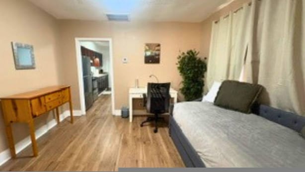 Een slaapkamer met een bed, een bureau, een stoel, een plant en een deur naar een badkamer.