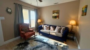 Een woonkamer met een plafondventilator, een bank, een stoel, een lamp en een schilderij aan de muur.