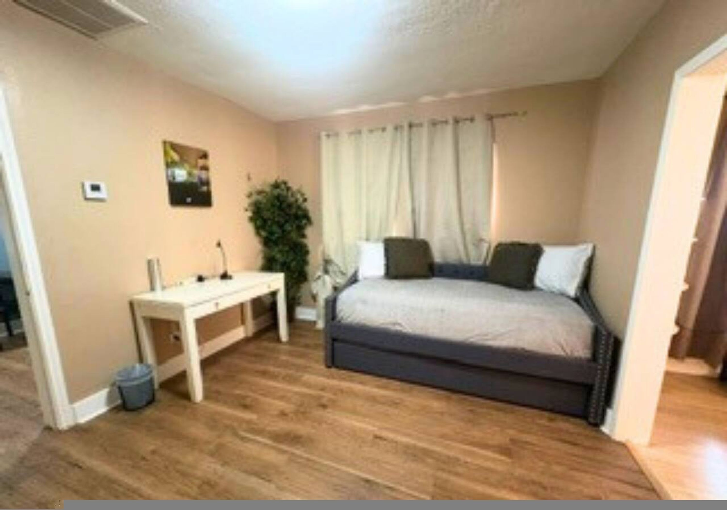 A bedroom with a bed, a bedside table, a lamp, a plant, and a window with curtains.