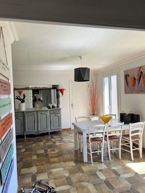 A dining area with a white table and chairs, a black pendant light, and a tiled floor. - Villa Papillon Clermont-Ferrand, 3-star, for 2 to 6 people, Clermont-Ferrand (Nohanent)