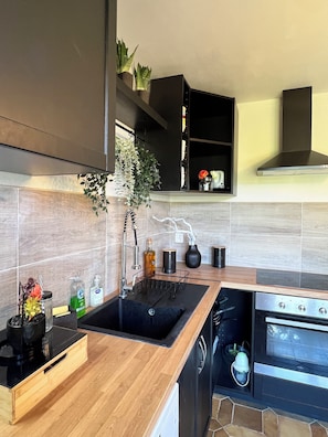 A modern kitchen with a black sink, wooden countertop, stainless steel appliances, and a black range hood. - Villa Papillon Clermont-Ferrand, 3-star, for 2 to 6 people, Clermont-Ferrand (Nohanent)