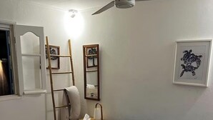 A bedroom with a bed, a nightstand, a lamp, a ceiling fan, a ladder, a framed picture, and a window. - Kaz HOLY LAND (Saint-Pierre)