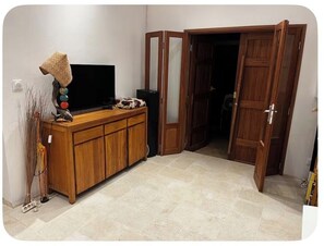 Ein Zimmer mit einem Holzschrank, einem Fernseher und einer Tür zu einem weiteren Raum.