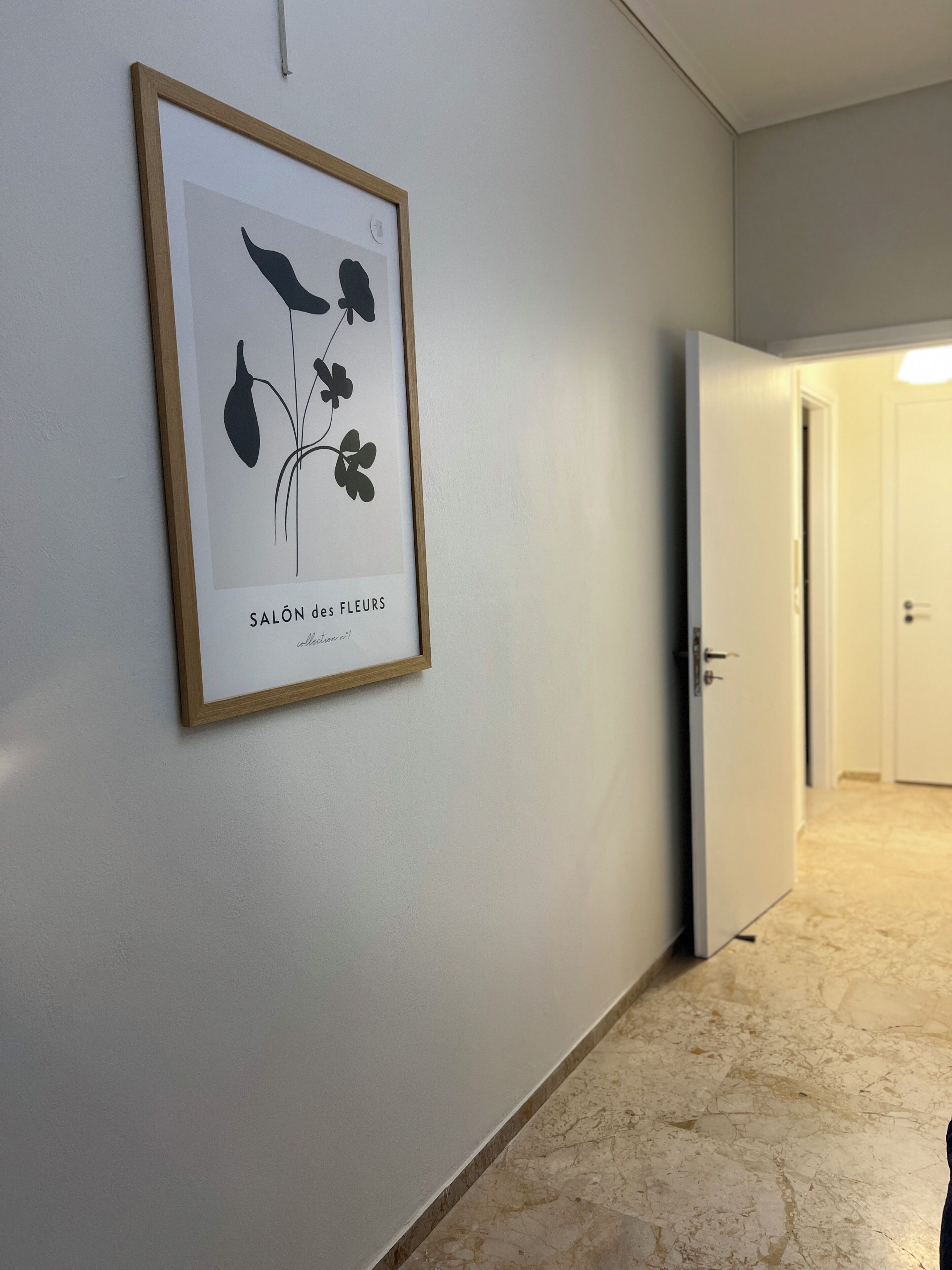 A hallway with a framed botanical illustration on the wall, a door, and a tiled floor.